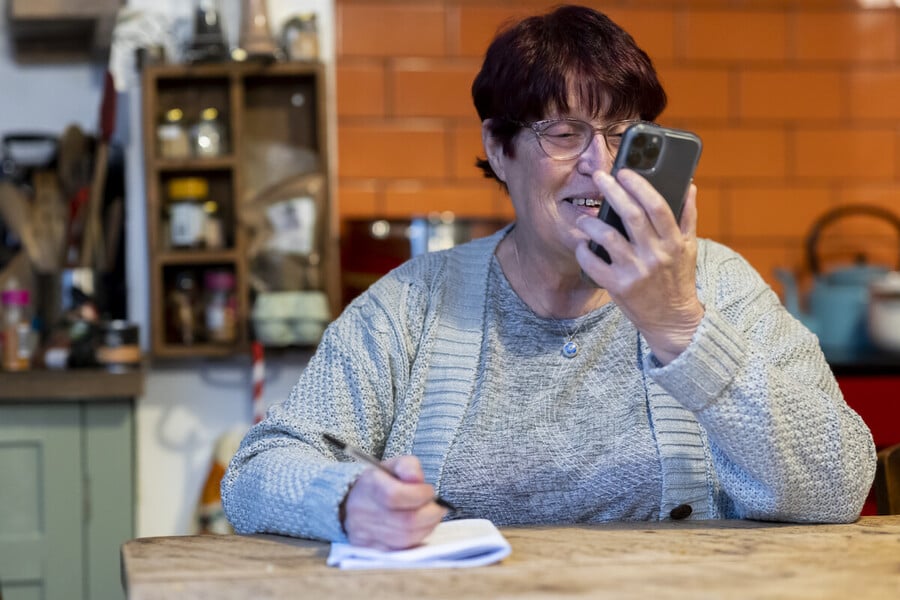 Woman using smartphone while taking notes at kitchen table