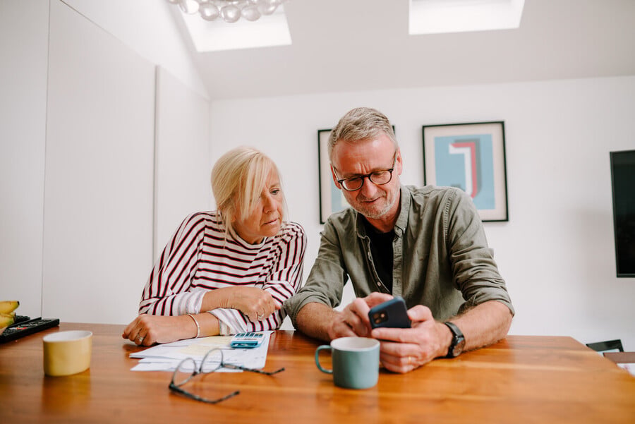 Couple reviewing paperwork and using smartphone at home