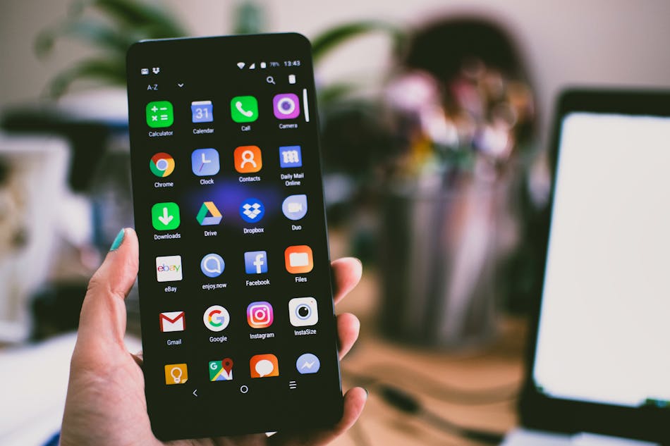 Hand holding smartphone displaying home screen with various app icons