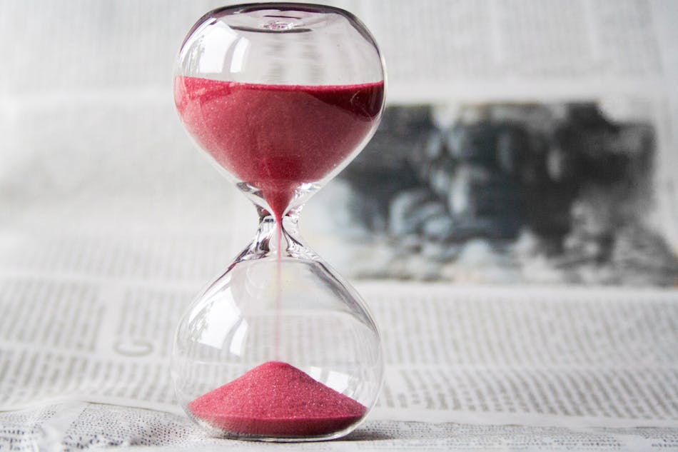 Red sand flowing through an hourglass on a textured surface